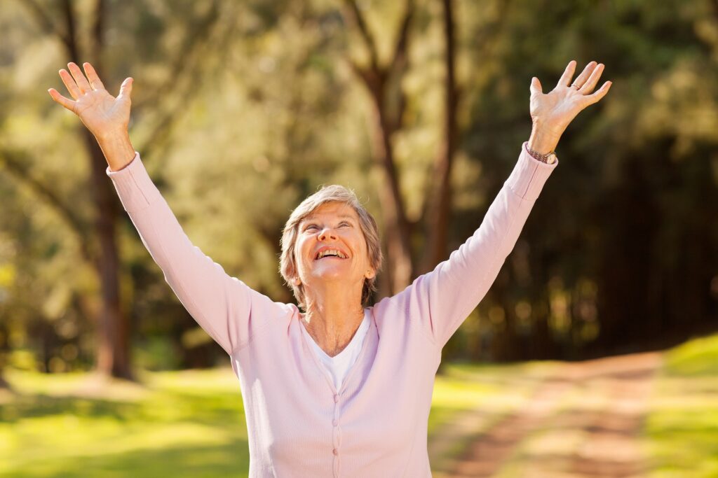 healthy elderly woman looking up with arms outstretched outdoors
